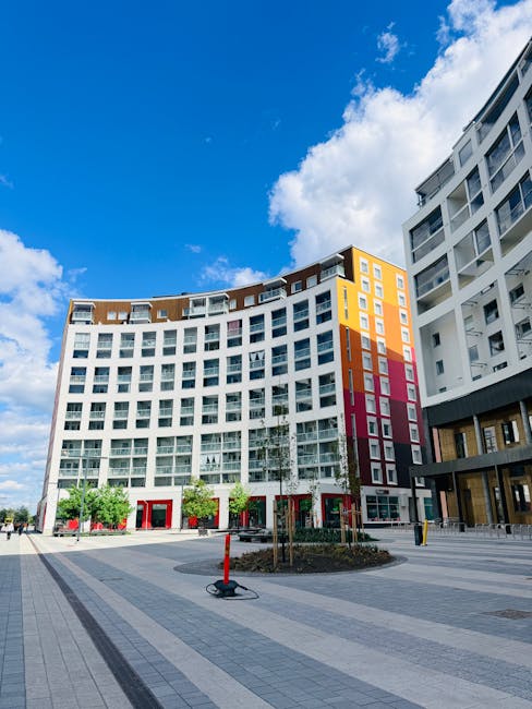 A modern residential building with a curved facade featuring multiple white-washed windows and colorful accents in yellow, orange, and pink along the upper floors. The ground level has red doorways, a