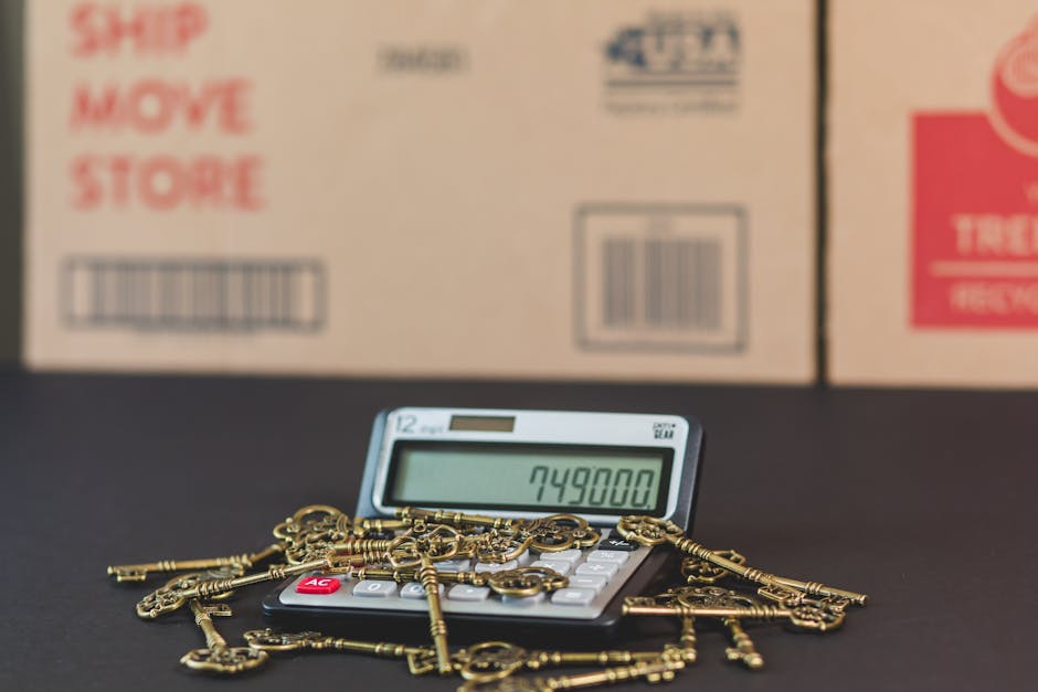 A flat lay image featuring a beige surface with various items related to home and office organization. Visible are a black calculator with white and pink buttons, a roll of black tape, a group of colorful index cards, a set of keys including a silver house key, a small silver house-shaped keychain, and a silver keyring. Additionally, there is a black marker, a pink measuring tape, and a document titled '7 Reasons to Own a Home' with blue text. In the background, there is a cardboard packing sheet with red 'FOLD TO HOLD' text and symbols indicating packaging instructions. The setting appears to be a workspace or organization area, emphasizing cleanliness and preparation, with natural lighting highlighting the neat arrangement of items. For surface cleaning and sanitisation of household or office spaces, Ilford Carpet Cleaners offers professional domestic cleaning services.